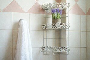 A bathroom with a white towel hanging on a rack, a decorative metal shelf with a plant, and a tiled wall with a geometric pattern. - Saranda Waterside Apartments (Sarandë)
