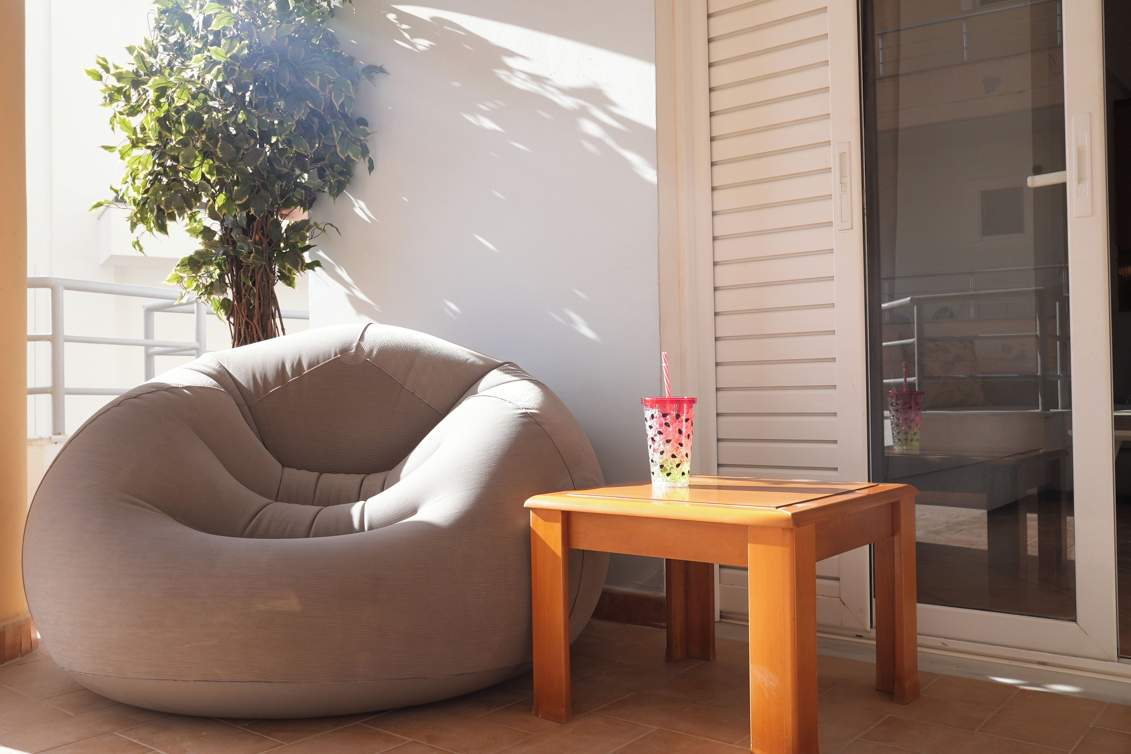 Une pièce avec un fauteuil en forme de poire de couleur beige, une table en bois et une plante en pot.