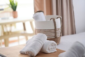 A neatly folded white towel on a wooden tray, a woven basket with a towel, and a bed in a well-lit room. - Saranda Waterside Apartments (Sarandë)