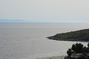 A coastal view with a calm sea, a small peninsula with vegetation, and a distant mountain range. - Saranda Waterside Apartments (Sarandë)