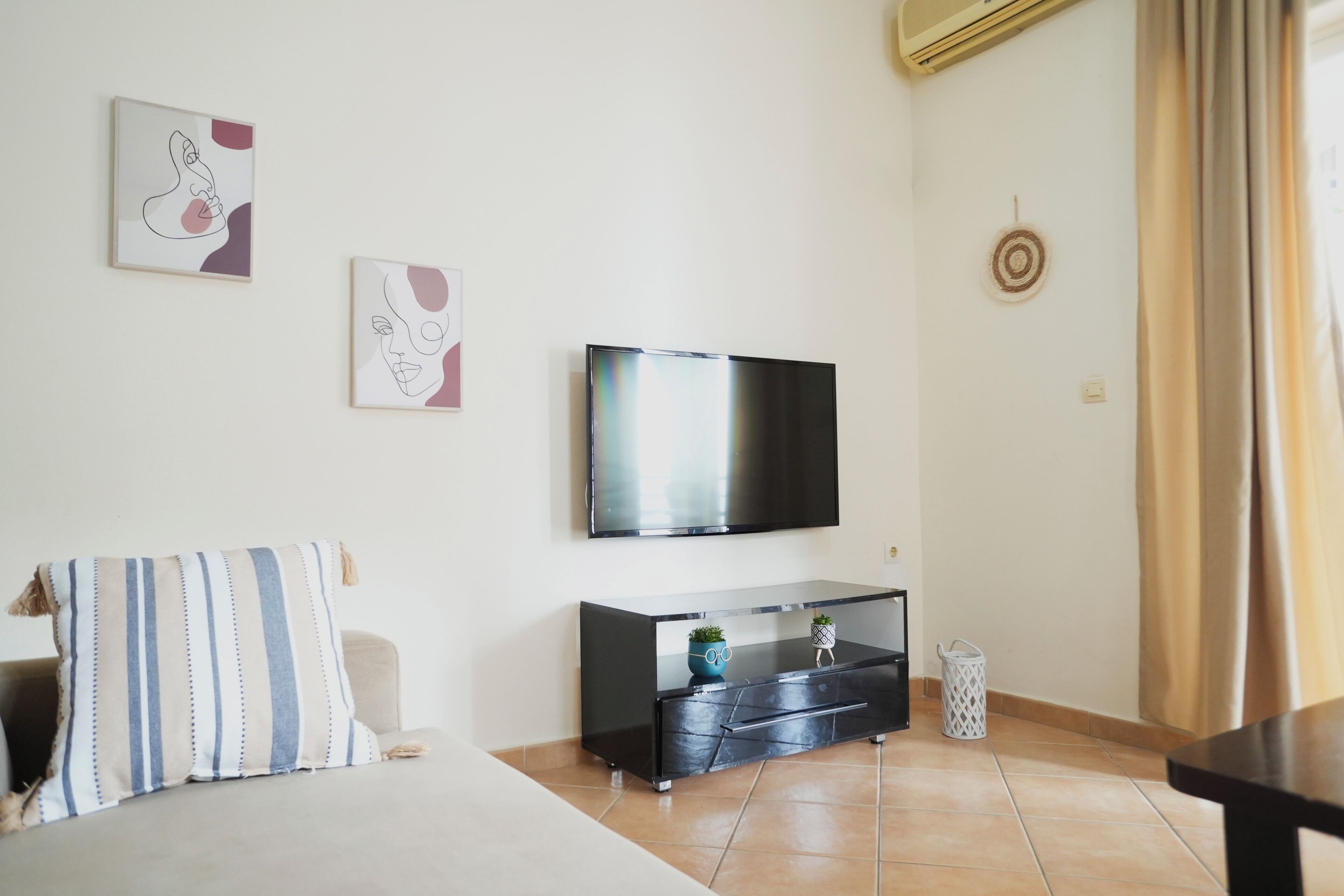 A modern living room with a flat-screen TV mounted on the wall, a black entertainment unit, and a striped pillow on the sofa.