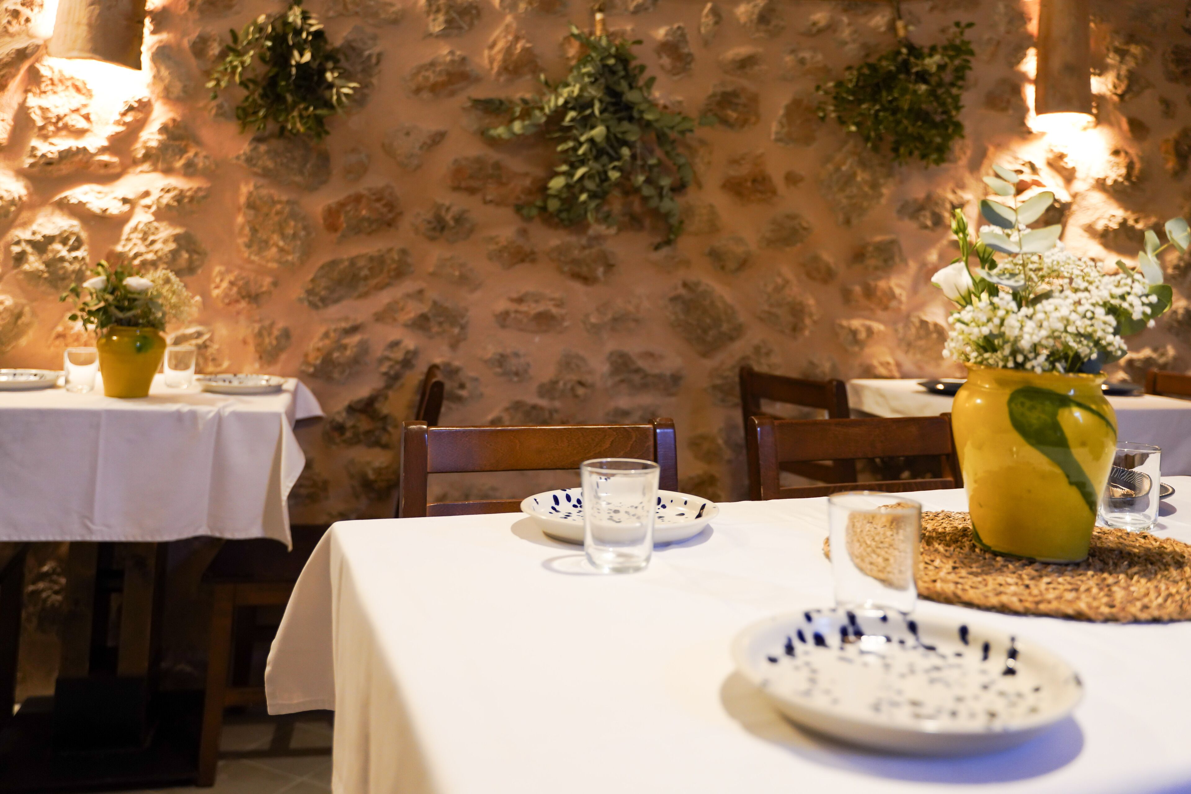 A dining table set with plates, glasses, and a yellow vase with flowers.