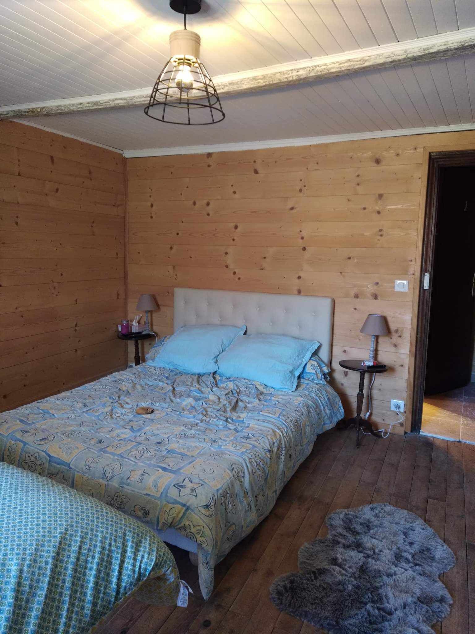 Ein Schlafzimmer mit Holzwänden, einem Bett, zwei Nachttischlampen und einer Hängeleuchte.