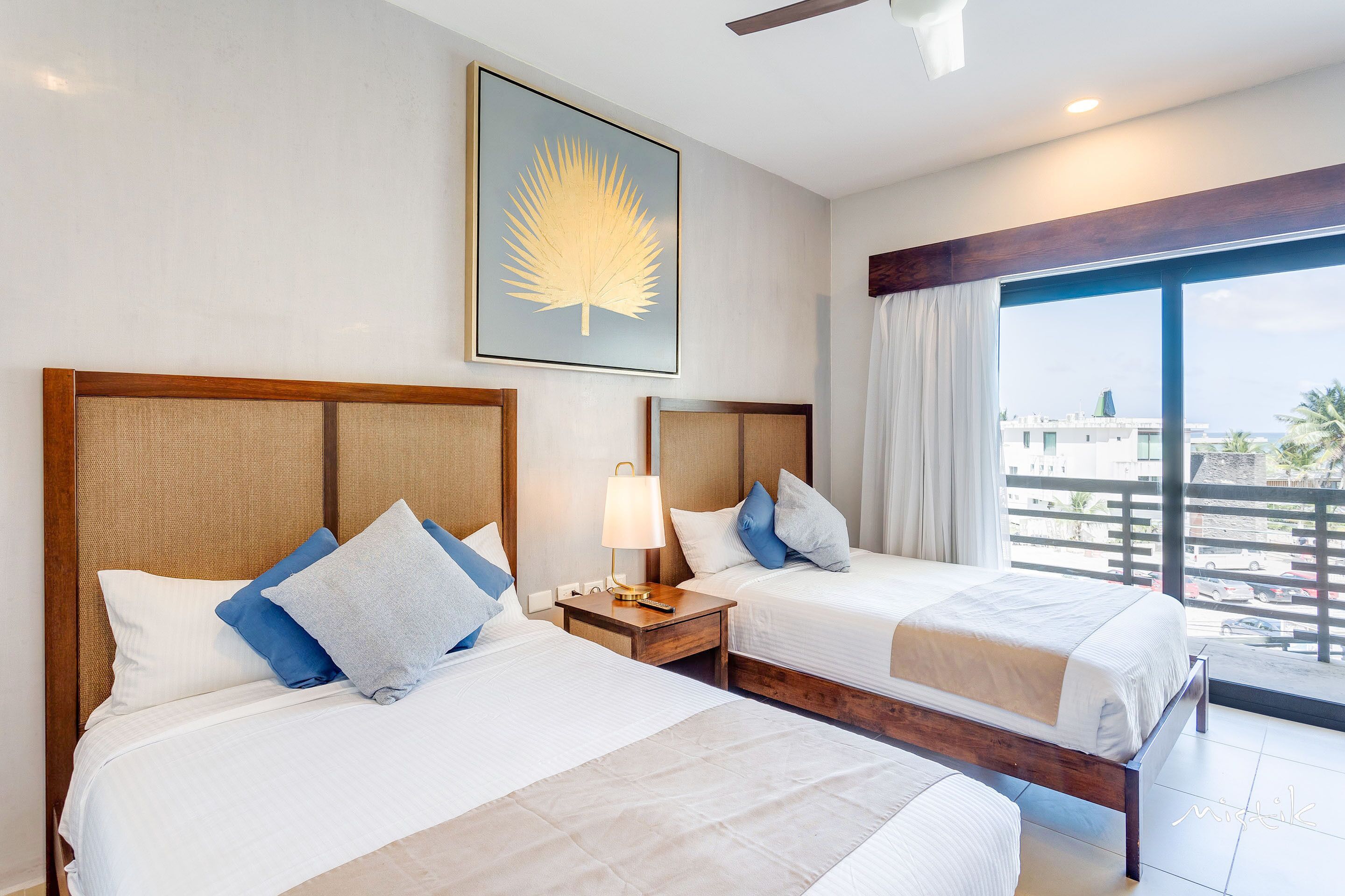 Quarto de hotel com duas camas, uma janela grande e vista, e um ventilador de teto.