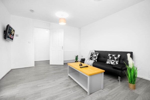 Una sala de estar moderna con una mesa de centro de madera, un sofá negro con cojines estampados y una planta en maceta.
