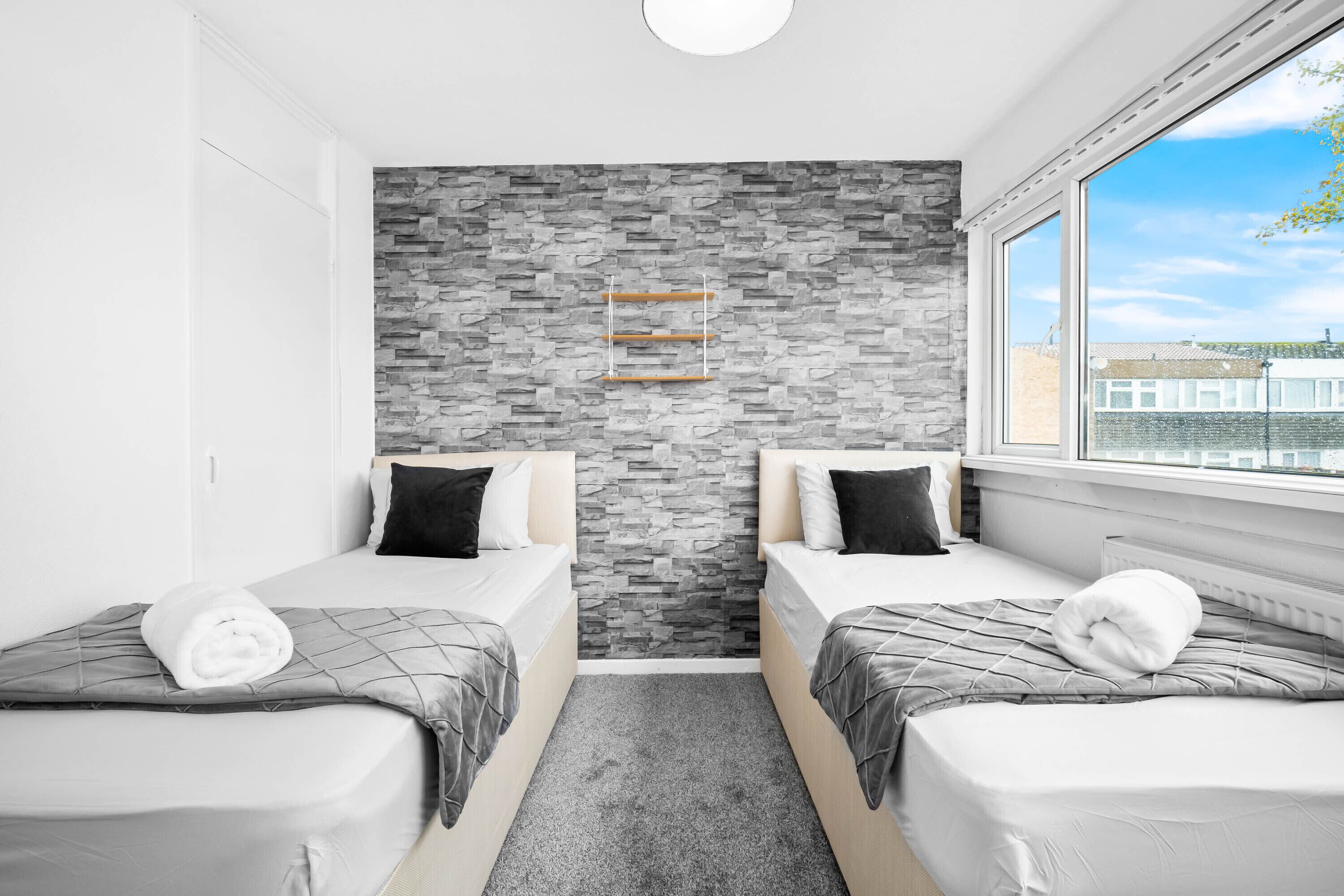 Een moderne hotelkamer met twee bedden, een wand met grijs patroon en een raam met uitzicht op de stad.