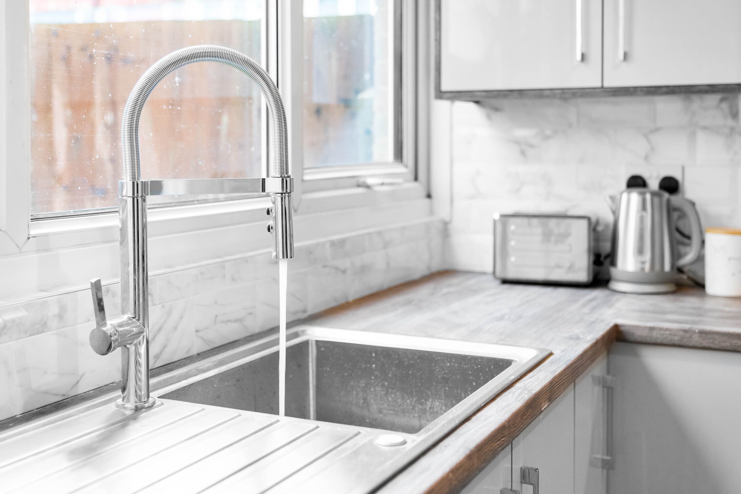 A modern kitchen with a stainless steel sink, a window, and a wooden countertop.