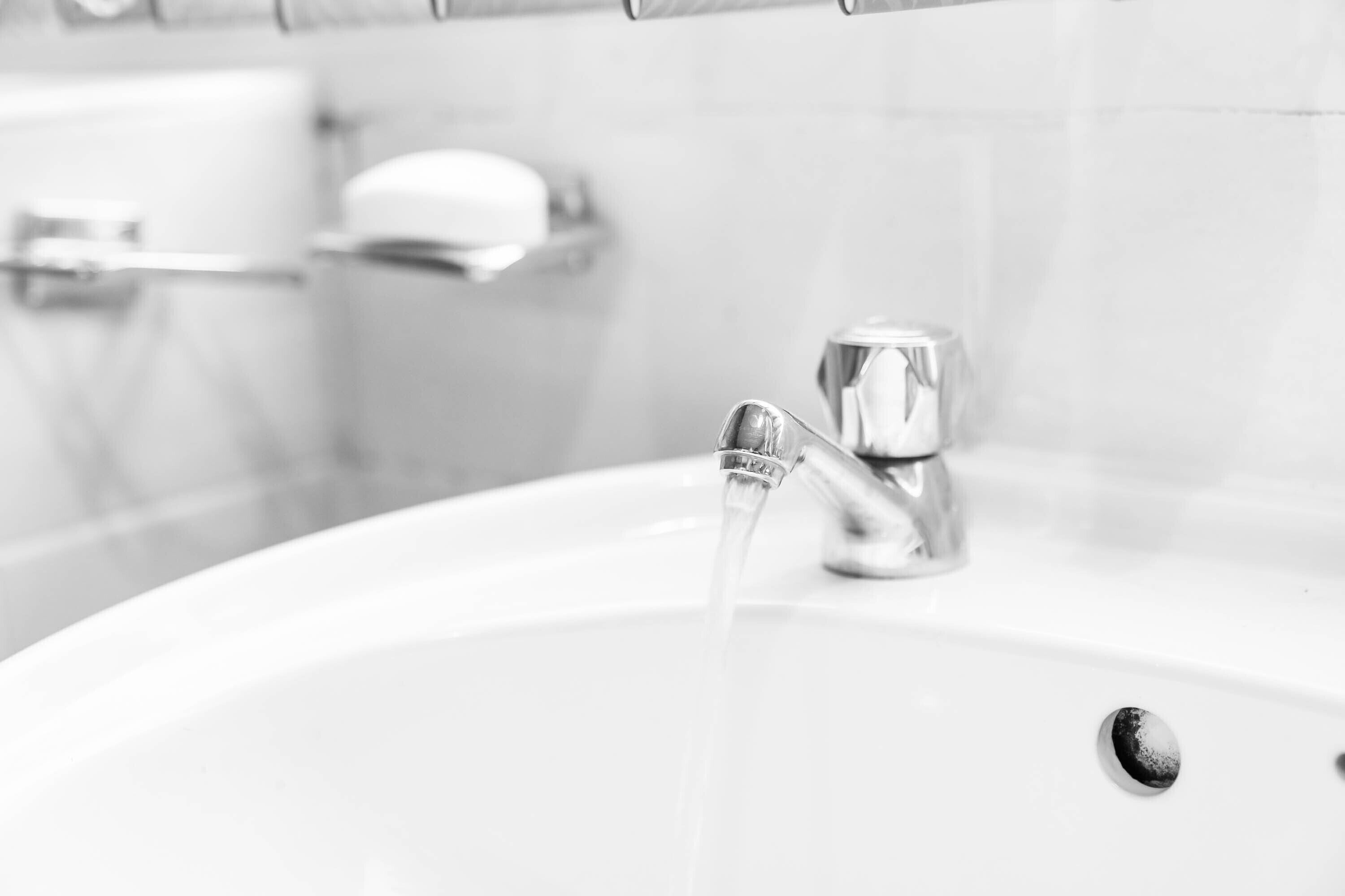 A bathroom sink with running water, a soap dish, and a toilet paper holder on the wall.