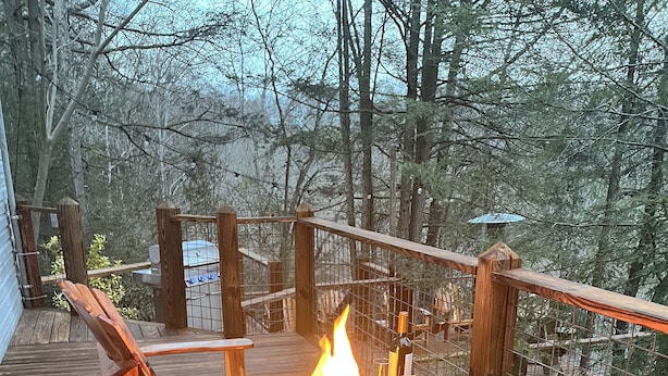 A deck with a fire pit, wooden chairs, and a railing overlooking a forested area. - NEW! On a WATERFALL! Fiery Gizzard Lodge at Sycamore Falls! 13 bluff acres!  (Tracy City)