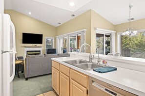 A modern kitchen with a built-in dishwasher, a grey sofa, and a flat-screen TV.