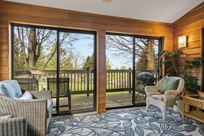 A room with a large sliding glass door leading to an outdoor deck, wicker furniture, and a patterned rug.