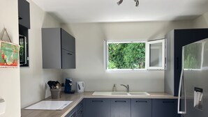 Une cuisine moderne avec des meubles gris, un réfrigérateur en acier inoxydable, une machine à café et une fenêtre donnant sur un paysage verdoyant.