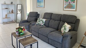 Un salon avec un canapé gris, une petite table basse en bois et un miroir. On y trouve des objets décoratifs sur des étagères et un tableau encadré au mur.