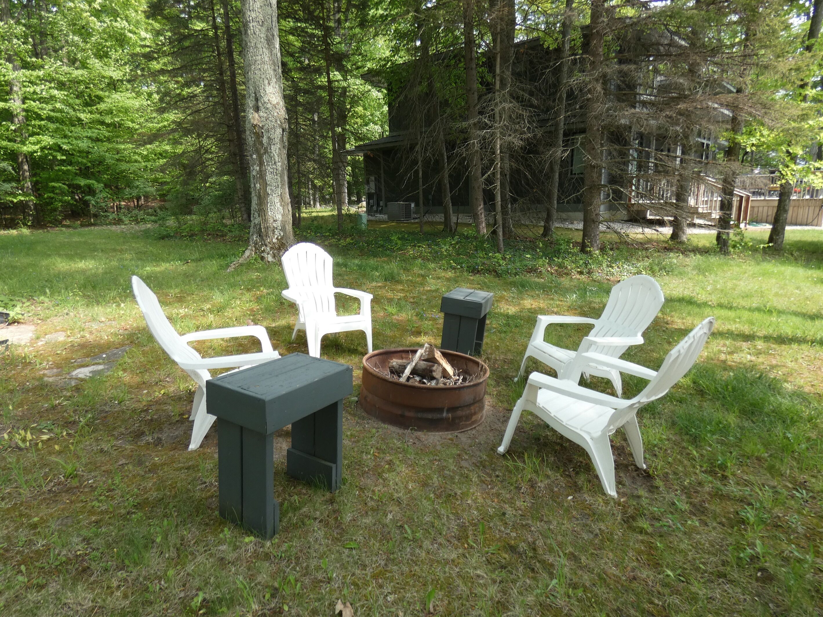 Un espacio al aire libre con sillas Adirondack blancas y una mesa, rodeado por un brasero y una terraza de madera.