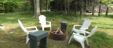 Un espacio al aire libre con sillas Adirondack blancas y una mesa, rodeado por un brasero y una terraza de madera.