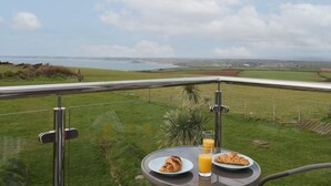 A table with breakfast items and a glass of orange juice on a balcony overlooking a coastal landscape. - 5 Ocean Reach (Kingsbridge)
