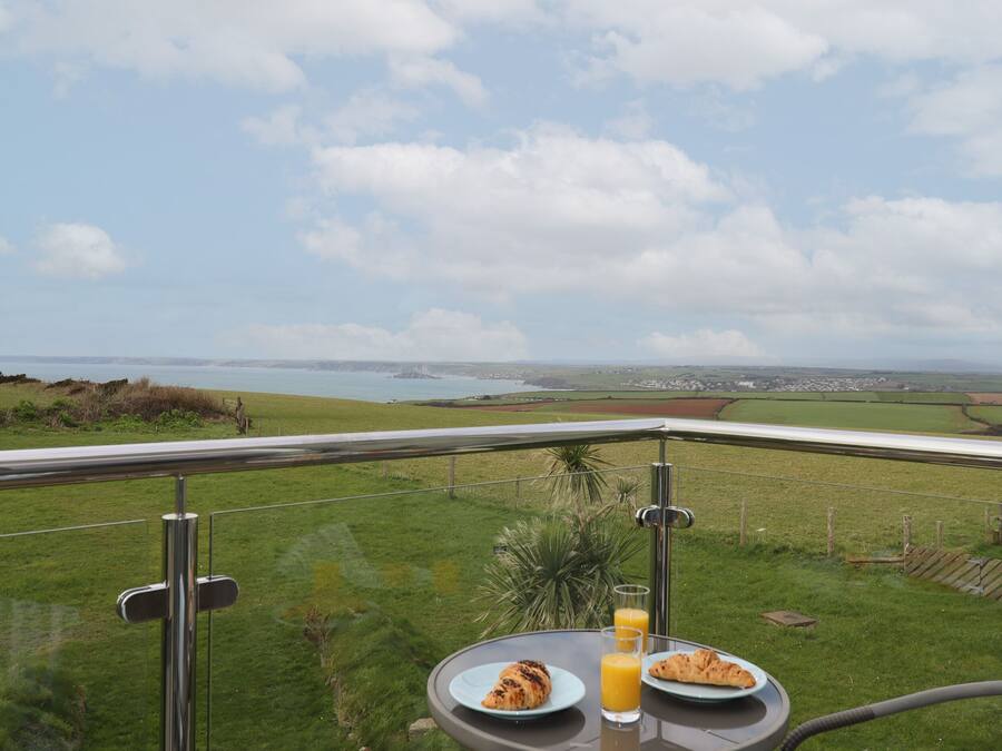 Une table avec des aliments pour le petit-déjeuner et un verre de jus d’orange, sur un balcon donnant sur un paysage côtier.