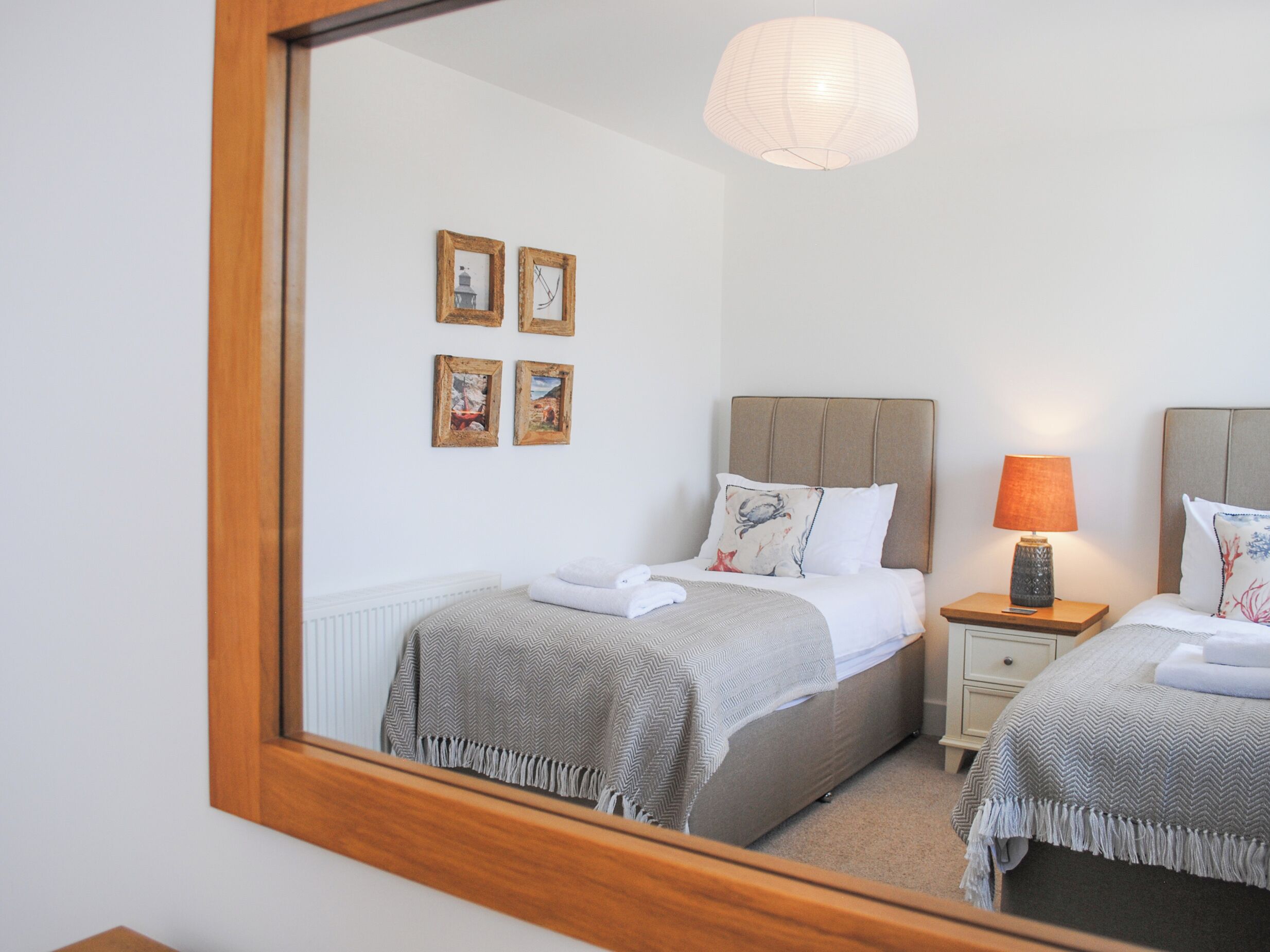 A bedroom with two beds, a nightstand with a lamp, and a mirror reflecting the room.
