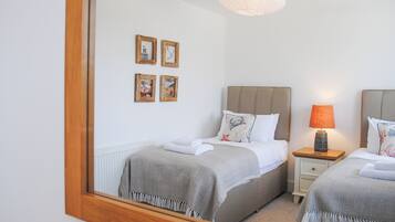 A bedroom with two beds, a nightstand with a lamp, and a mirror reflecting the room.