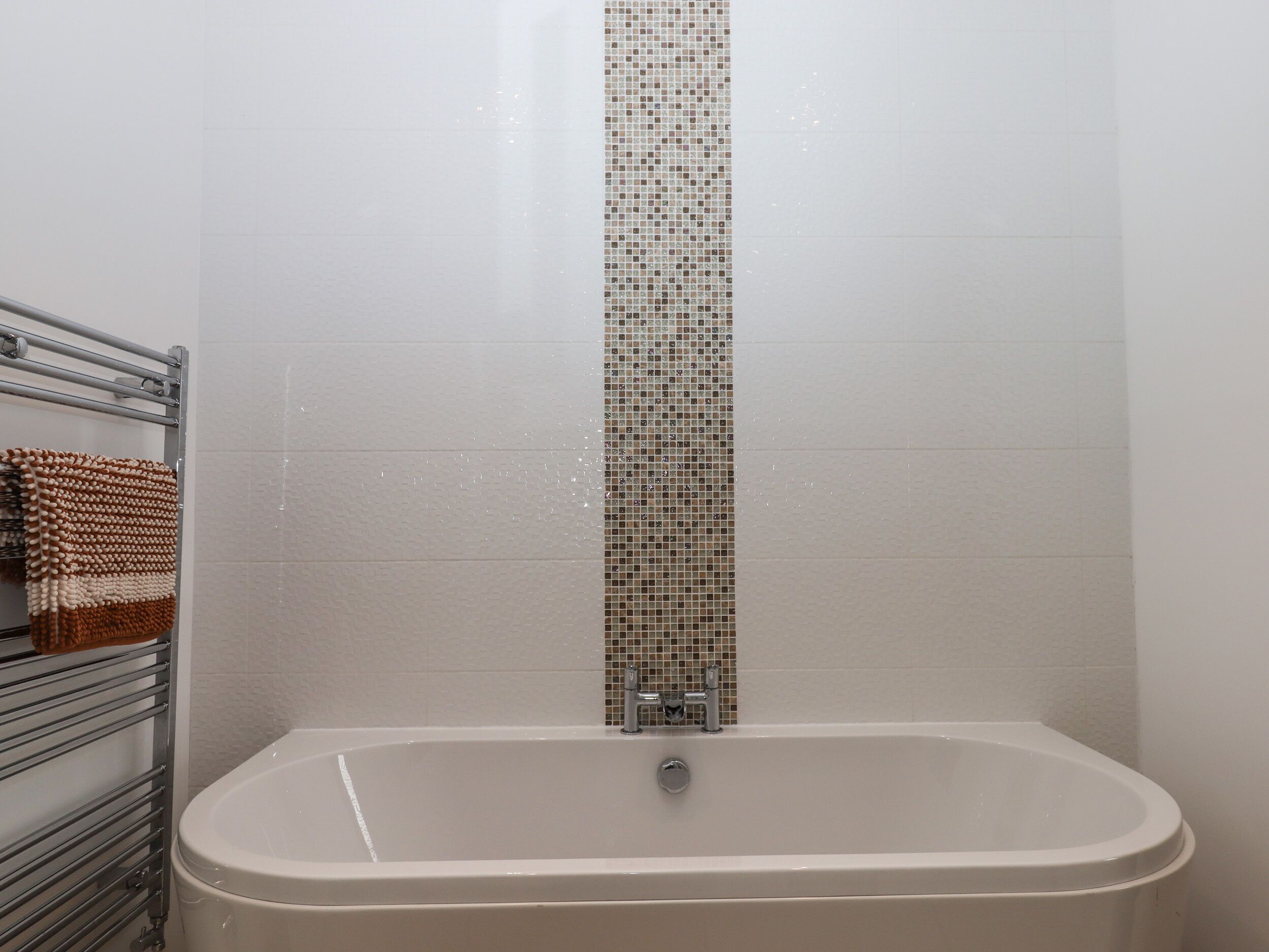 A bathroom with a bathtub, a towel rack with a towel, and a tiled wall.
