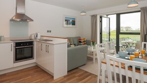 A modern kitchen with a built-in oven, a dining area with a table and chairs, and a large window offering a view of the outdoors. - 5 Ocean Reach (Kingsbridge)