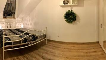 Ein Schlafzimmer mit einem Bett, Holzboden, einer an der Wand befestigten Ablage mit Dekoration und einem Deckenventilator.