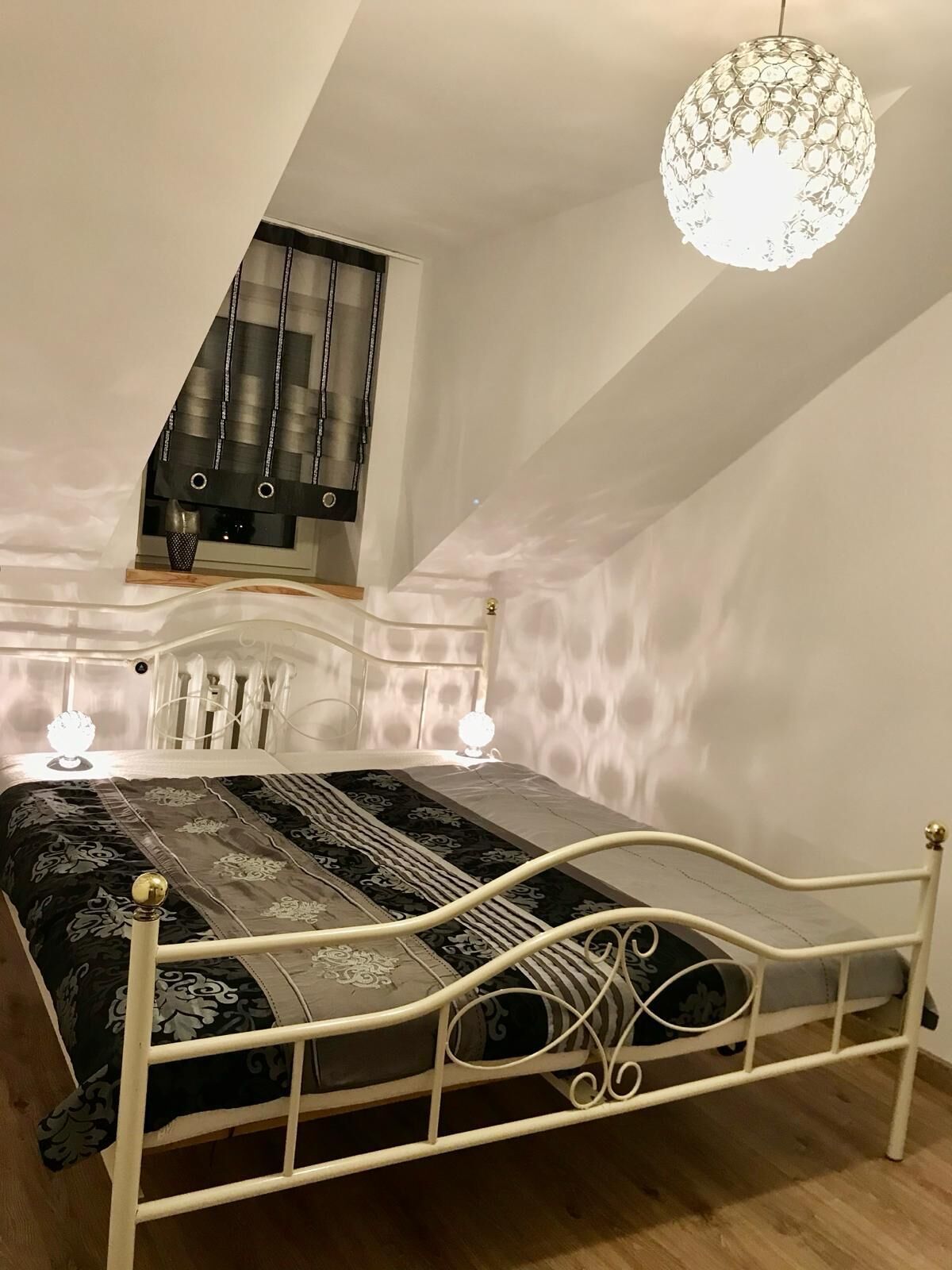 Un dormitori amb un llit, dues làmpades de nit, una pèndol i un sostre inclinat.