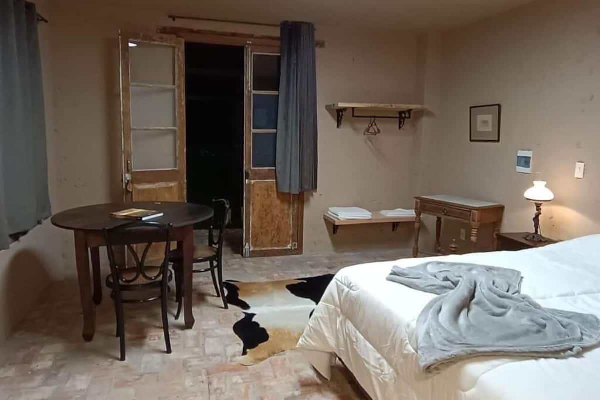 Quarto de hotel com cama, escrivaninha, cadeira, mesa e porta.
