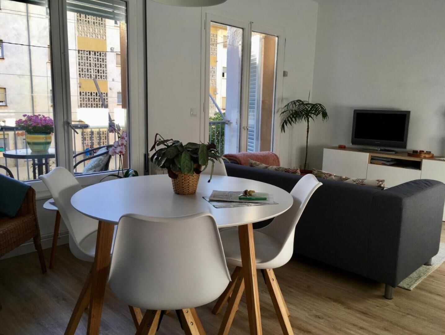Een moderne woonkamer met een ronde eettafel, witte stoelen, een grijze bank en een televisie op een wit kastje.