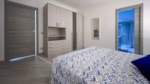 Une chambre à coucher avec un lit, une armoire et une salle de bain visible à travers une porte ouverte.