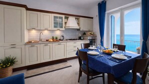Une cuisine moderne avec des meubles blancs, un coin repas avec une nappe bleue et une vue sur la mer.