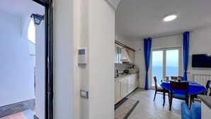 Une cuisine moderne avec des meubles blancs, un coin repas doté d’une table et de chaises bleues, et une vue sur la mer grâce à de grandes fenêtres.