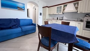 Un espace de vie compact comprenant un canapé bleu, une table à manger recouverte d’une nappe bleue et un coin cuisine avec des meubles blancs et une cuisinière blanche.