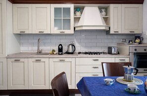 A kitchen with white cabinets, a gas stove, a coffee maker, and a table set with cups and saucers.