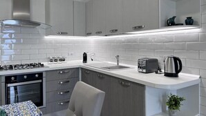 A modern kitchen with white cabinetry, a stainless steel range hood, a built-in oven, a sink, and a countertop with a toaster and kettle. - Villa Giulia lovely view #2 (Amalfi)