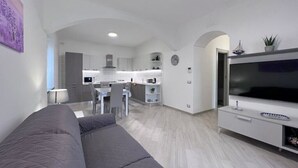 A modern living room with a grey sofa, a TV, and a kitchen in the background. - Villa Giulia lovely view #2 (Amalfi)