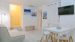 A modern, well-lit room with a sofa, a dining table with chairs, a TV mounted on the wall, and artwork on the walls. - A due Passi dal Molo by Wonderful Italy - Apartment (Cefalù)