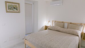 A bedroom with a bed, bedside tables, an air conditioner, a door, and a wall-mounted light fixture. - A due Passi dal Molo by Wonderful Italy - Apartment (Cefalù)