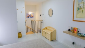 A modern interior with a wooden bench, a small shelf with decorative items, and a framed painting on the wall.