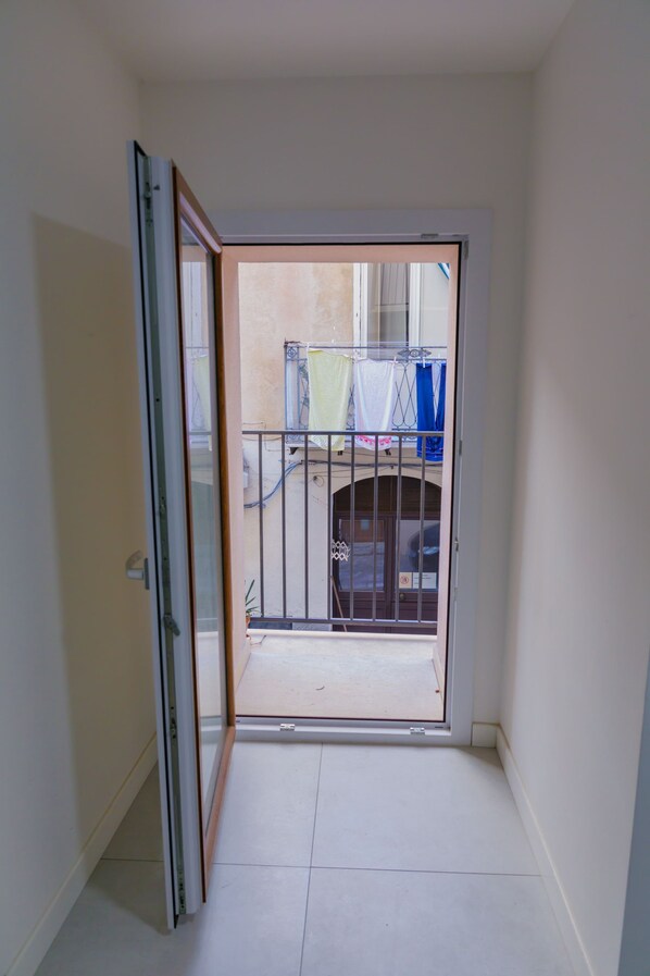 A narrow hallway with a door leading to a balcony. The balcony has a metal railing and a view of a building with laundry hanging outside. - A due Passi dal Molo by Wonderful Italy - Duplex (Cefalù)