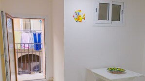 A small, bright room with a white table and chairs, a bench, and a door leading to a balcony with a view.