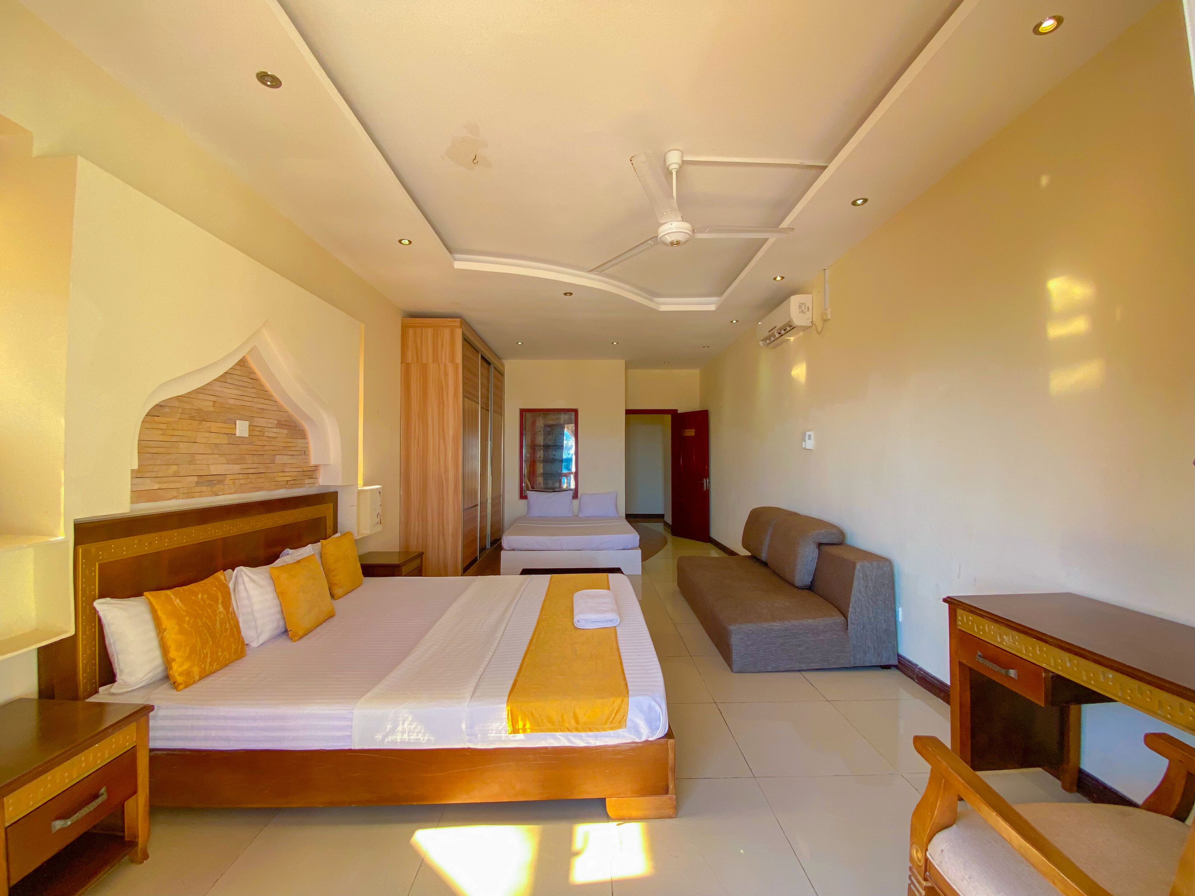 A hotel room with two beds, a sofa, a desk, and a wooden headboard.