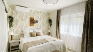 A bedroom with a bed, bedside tables, a wall-mounted air conditioner, a decorative wall piece, a window with curtains, and a wooden floor. - Willkommen in der Villa Dobri Dupin, Ihrem Perfekten Urlaubsdomizil am Strand! (Posedarje)
