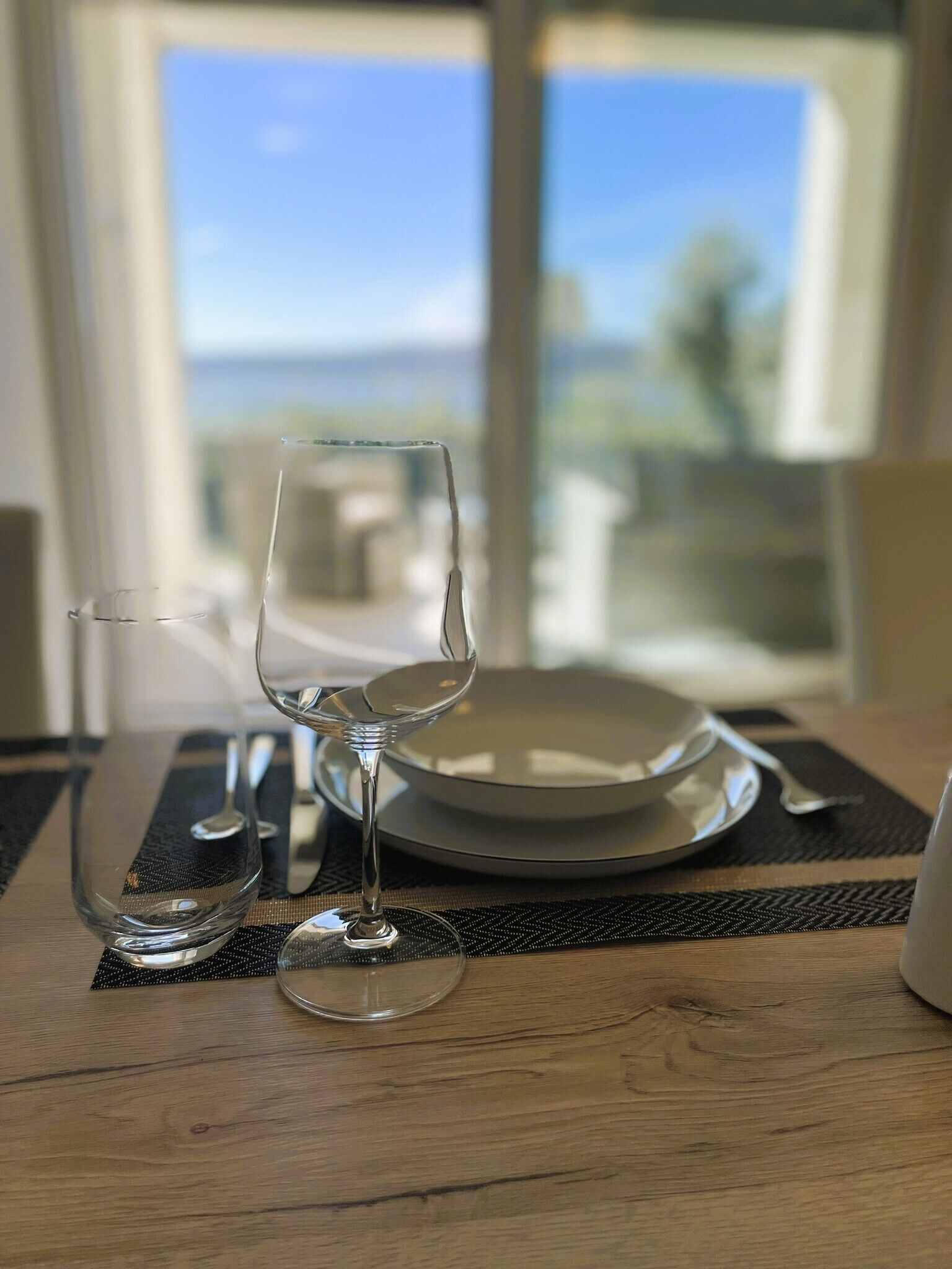 Een tafel met een wijnglas, een bord en een kom, geplaatst op een geweven tafelmat.