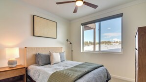 A bedroom with a bed, a nightstand, a floor lamp, a ceiling fan, a window with a view of a snowy landscape, and a framed picture on the wall. - 2 Mi to Fraser Tubing Hill: Condo w/ Fireplace! (Fraser)