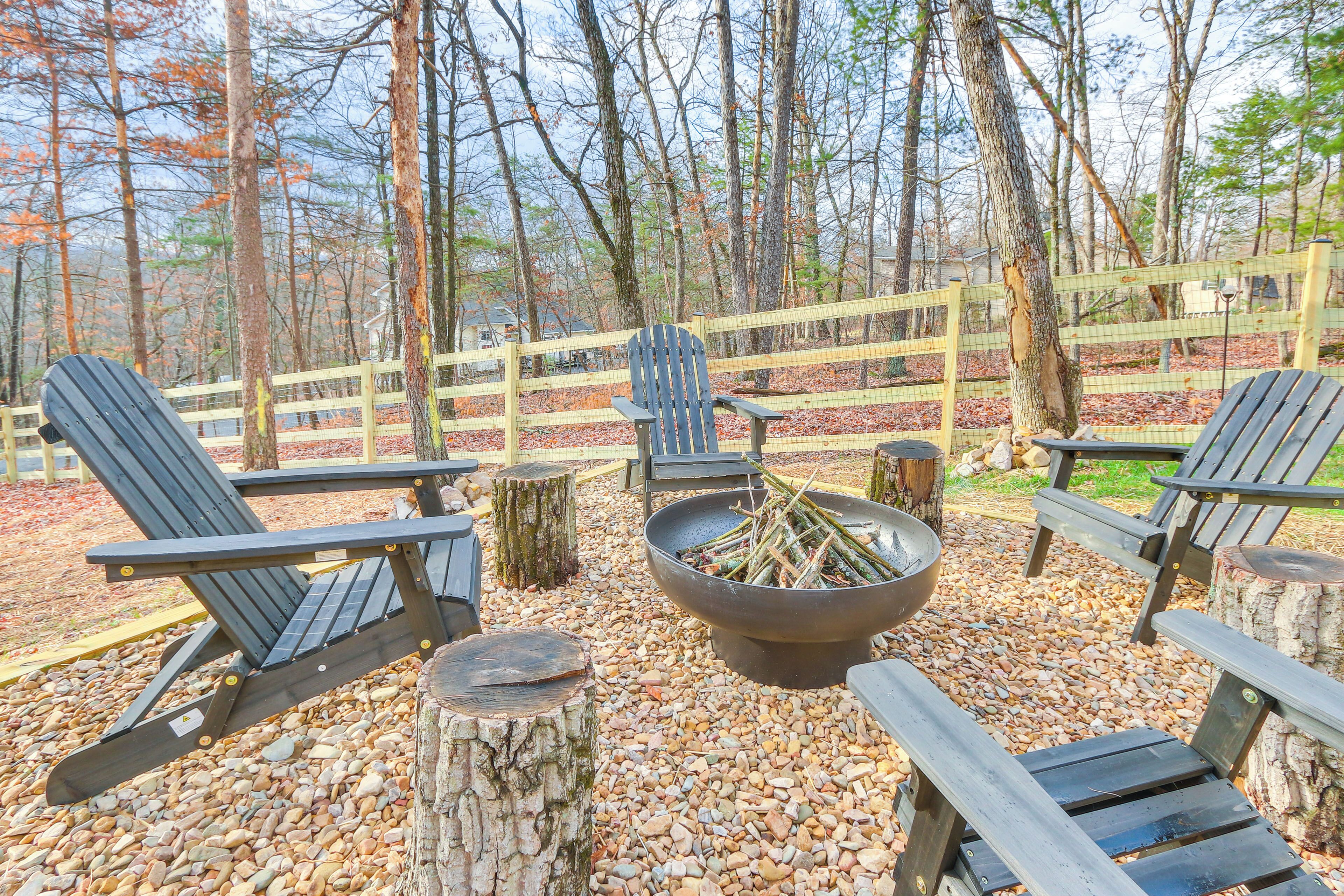 A wooden deck with Adirondack chairs and a fire pit surrounded by a wooden fence and trees.