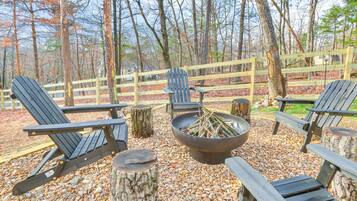 A wooden deck with Adirondack chairs and a fire pit surrounded by a wooden fence and trees.