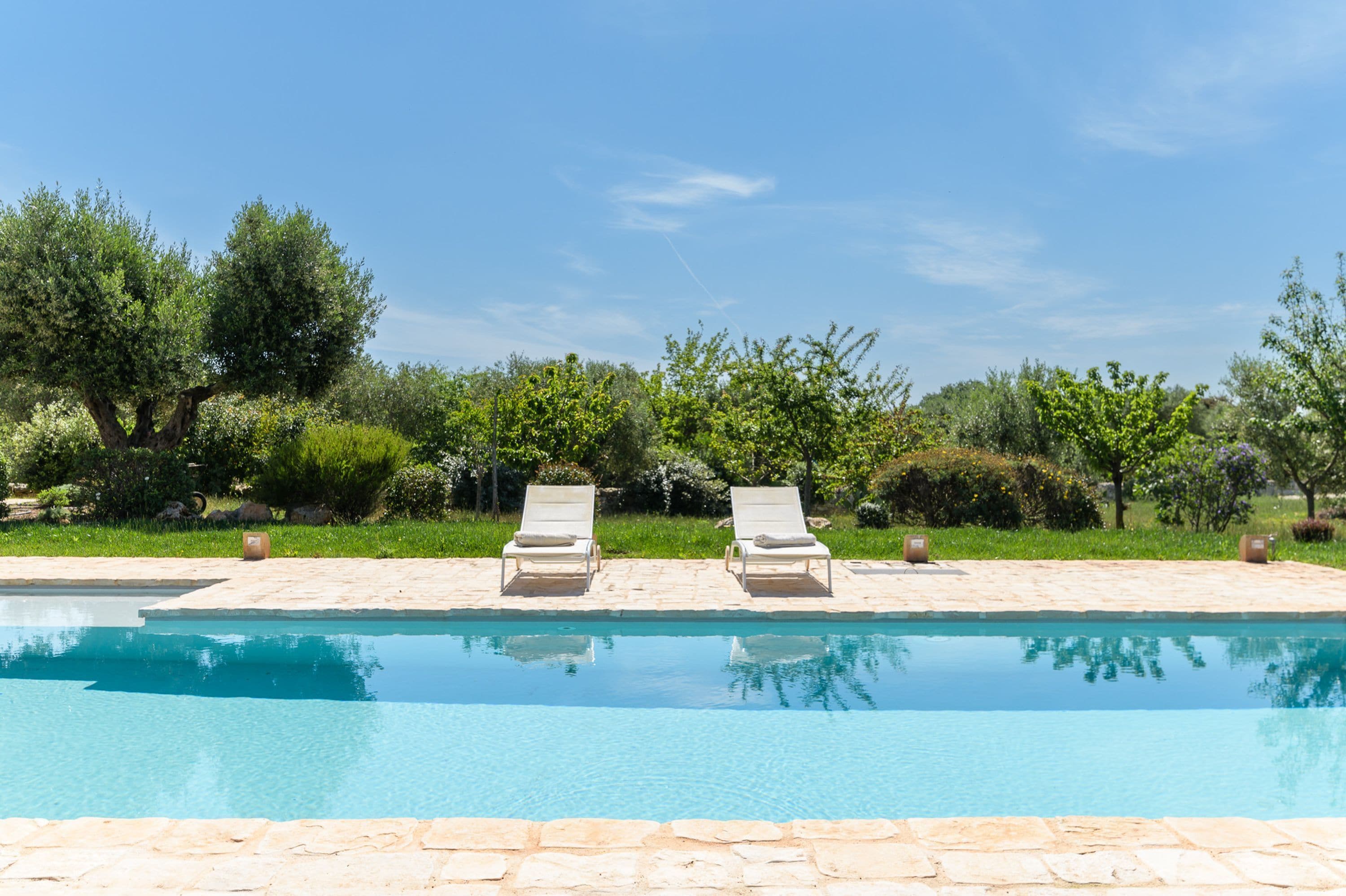 A swimming pool with two lounge chairs and a stone deck.