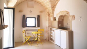 Una cocina compacta con un arco de piedra, un pequeño comedor con sillas amarillas y una ventana con cortinas.