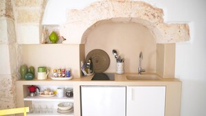 Una cocina compacta con un lavamanos integrado, un refrigerador y estantes con vajilla y utensilios de cocina.